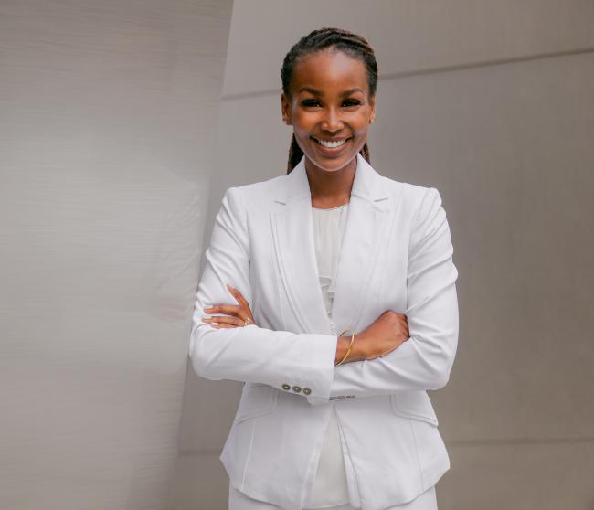 Female executive in a white suit standing with her arms crossed in front of a gray wall