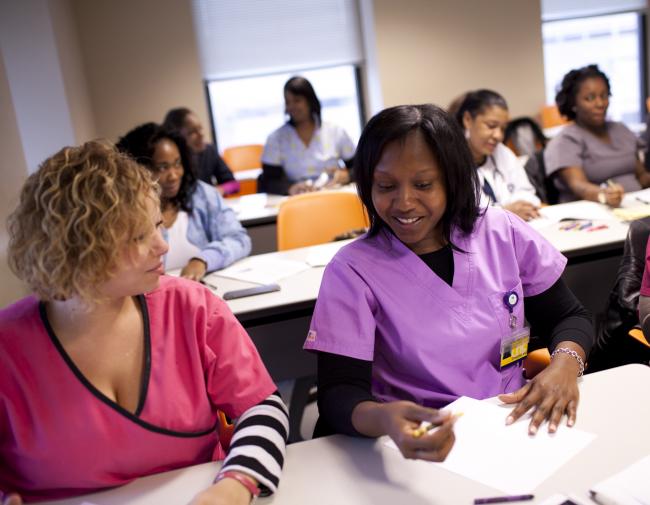 A group of women wearing scrubs, sitting in a classroom at University City District.