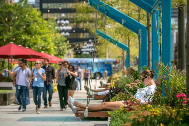 A woman lounging on a park swing in University City District, surrounded by flowers in bloom.